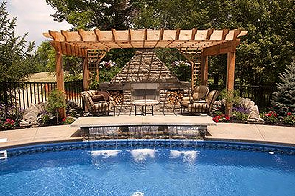 Cedar pergola and stone seating beside a gunite pool with waterfall spillways, built by Moss Landscaping